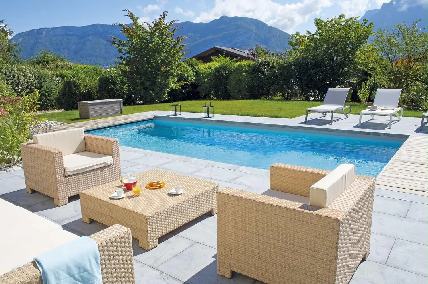 Piscine Desjoyaux avec dallage clair, salon de jardin et vue dégagée sur les montagnes