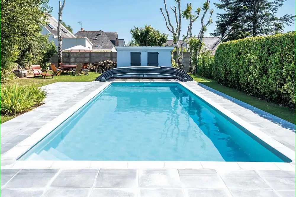 Piscine Desjoyaux rectangulaire équipée d'un abri bas, bordée d'une haie
